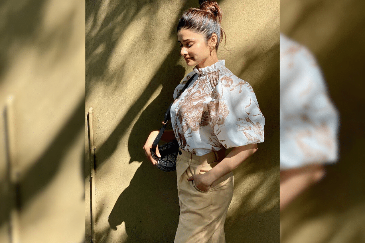 Chic And Breezy: Prachi looked poised in a white floral print ruffle top which she elegantly paired with tan-coloured high-waisted trousers and a snakeskin saddle bag. Lastly, she styled her hair in a sophisticated top knot bun and opted for dewy makeup and embossed gold studs. (Photo Courtesy: @prachidesai)
